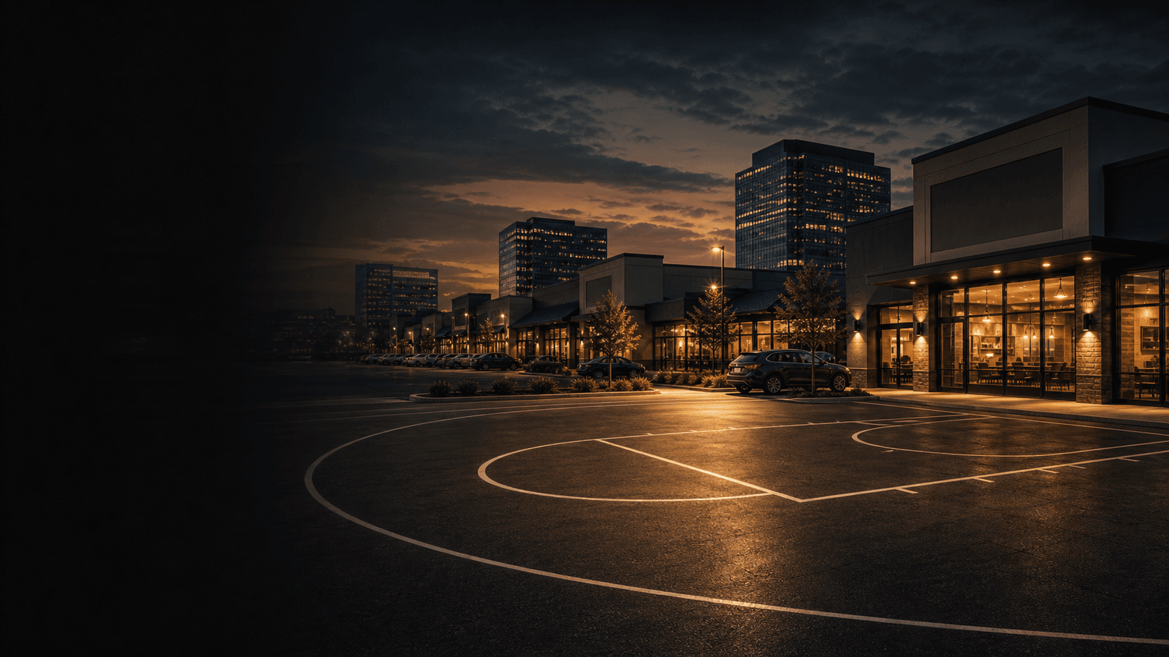 Commercial retail district at dusk with basketball court markings painted across the parking lot